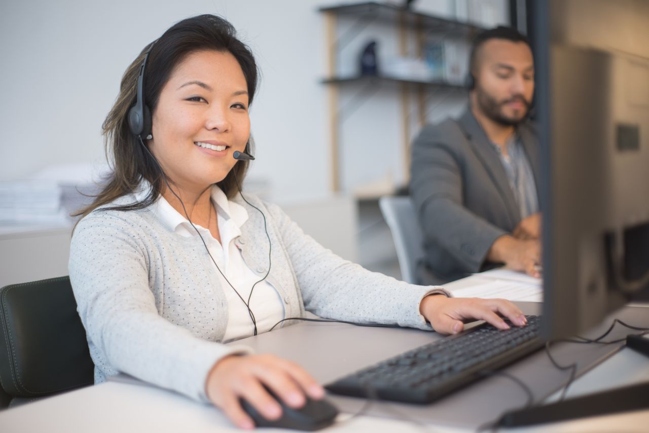 about-bg Two call center employees working with headsets in a modern office setting.